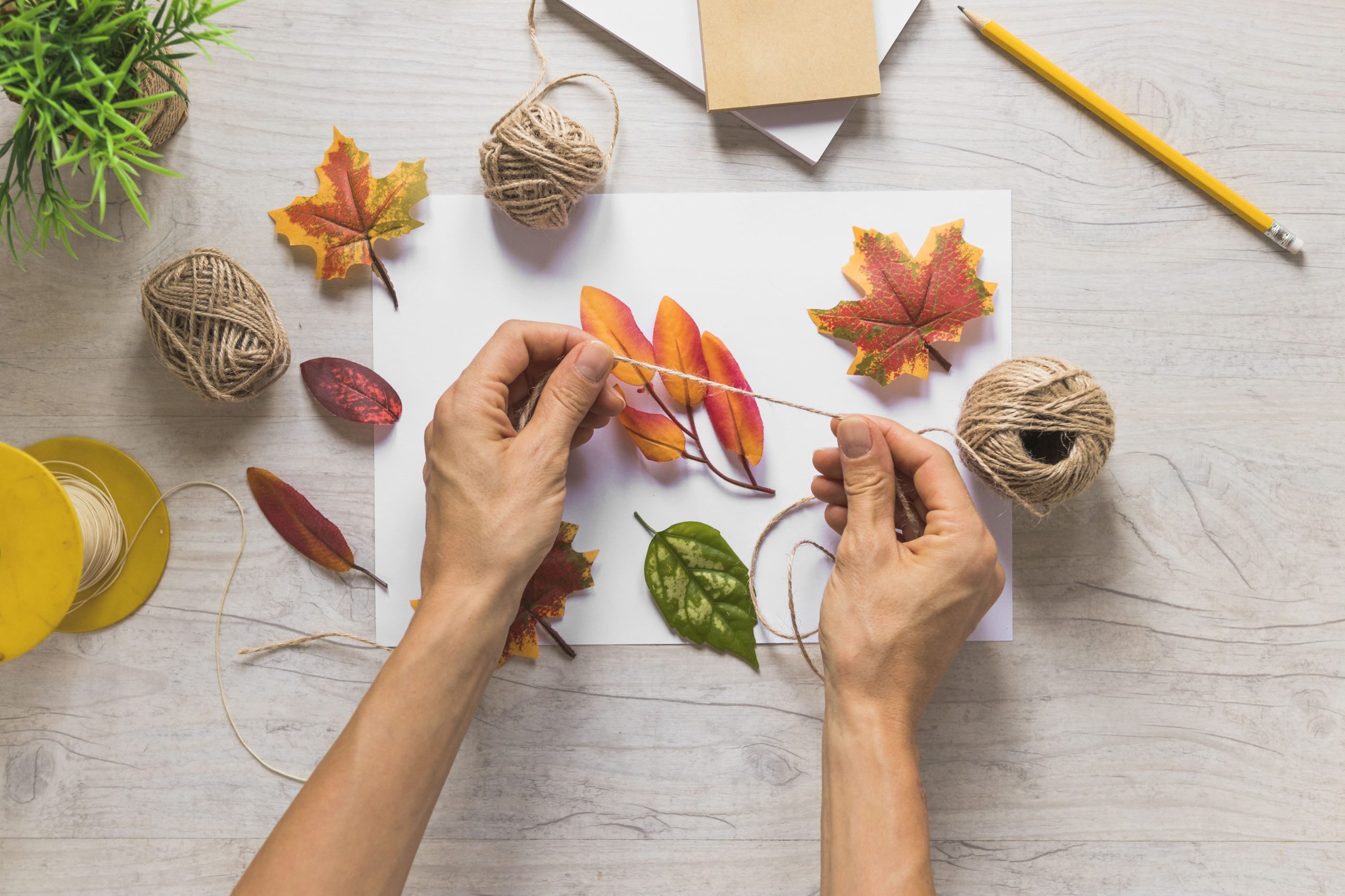person-using-string-with-fake-autumn-leaves-wooden-background-min