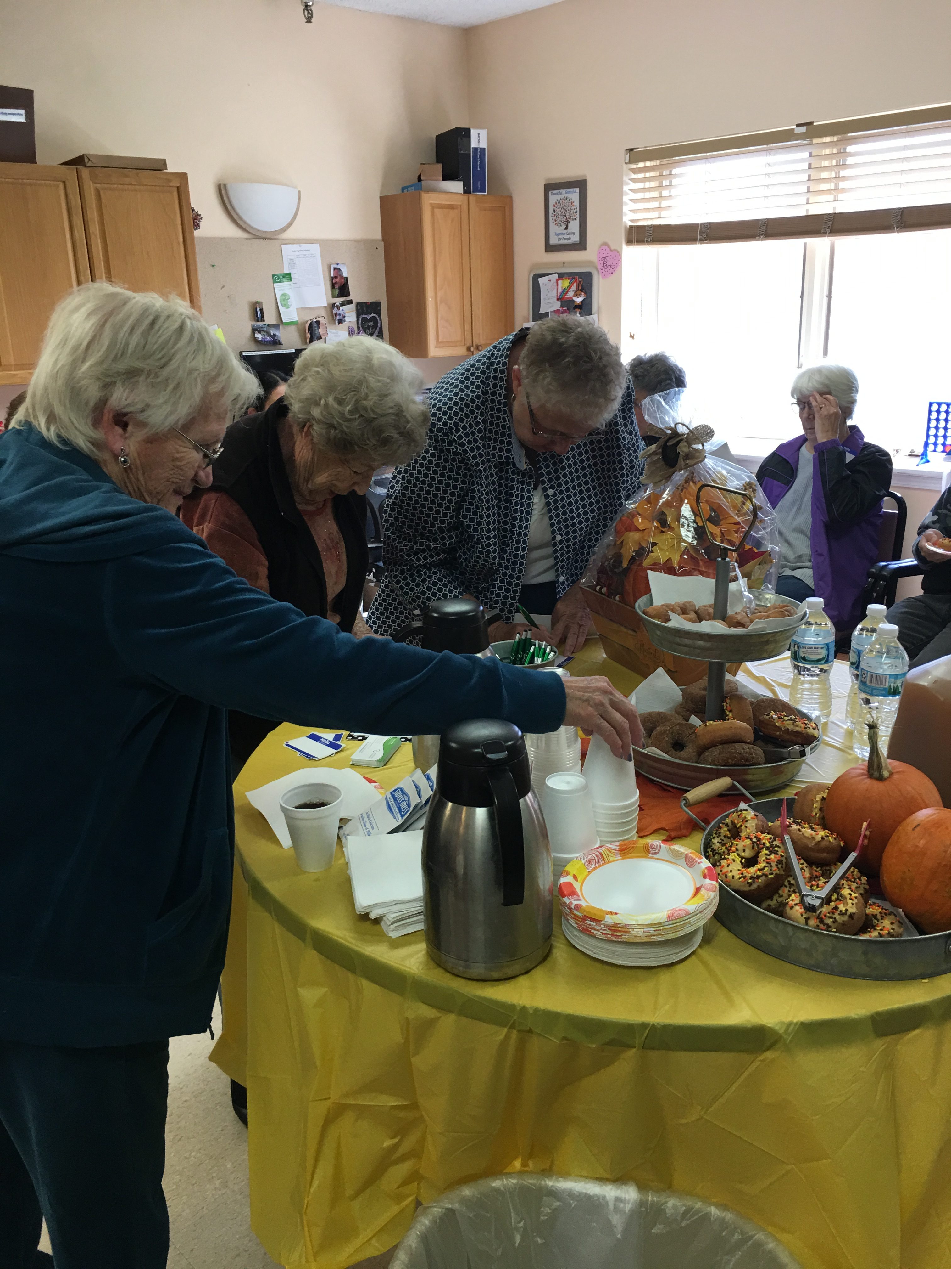 people reaching for cups and around table with pumpkins and donuts
